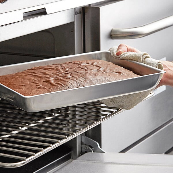 A person holding a Choice rectangular cake pan out of an oven.