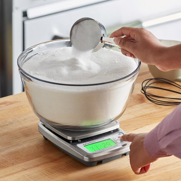 A person measuring white powder in a bowl on a digital scale.