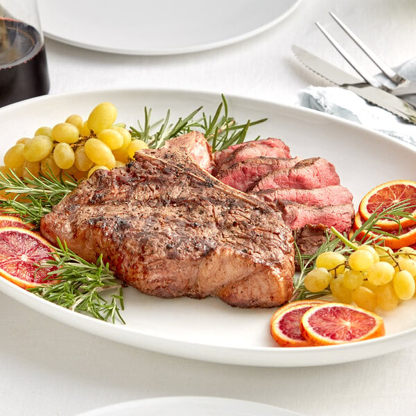 A plate of Rastelli's bone-in porterhouse steak with orange slices and grapes.