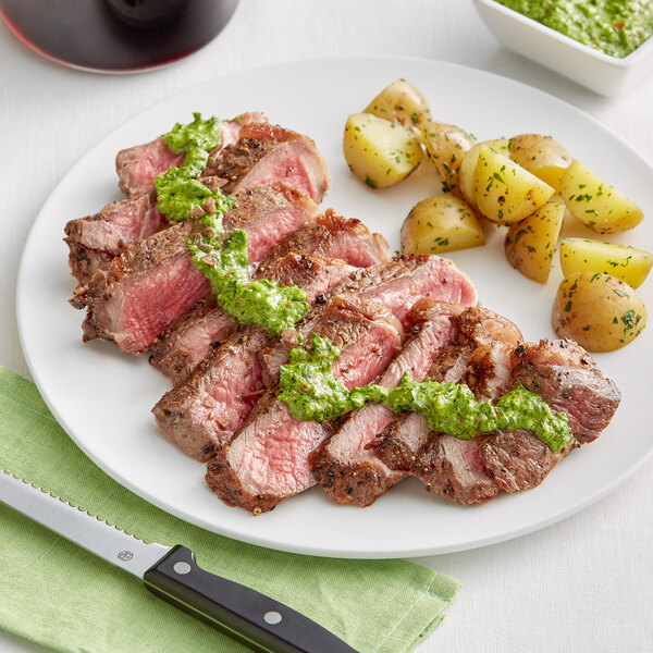 A plate with a Rastelli's USDA Prime New York Strip Steak and potatoes with green sauce.