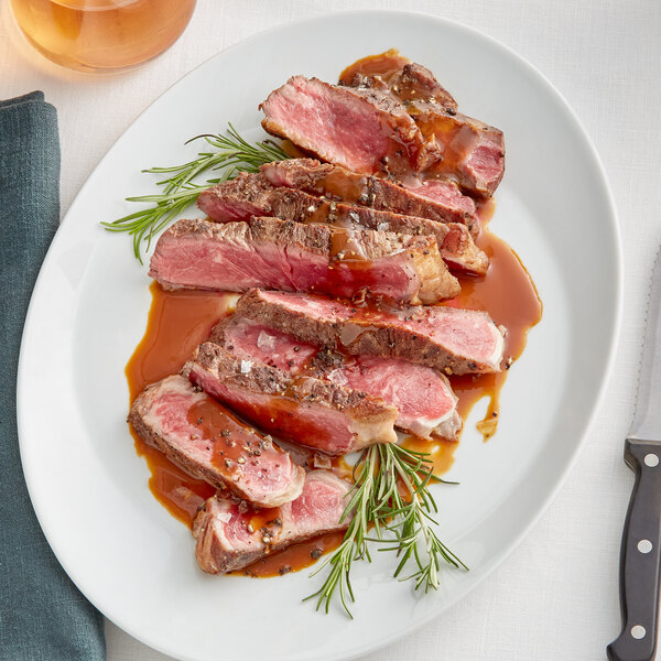A white plate with Rastelli's Black Angus New York Strip Steak topped with sauce and rosemary.