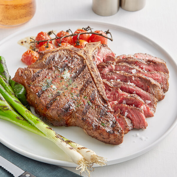 A plate with a Rastelli's USDA Prime Bone-In Porterhouse Steak, asparagus, and tomatoes.