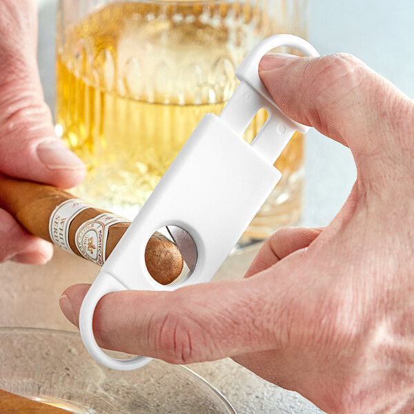 A hand using a Franmara white cigar cutter to cut a cigar.