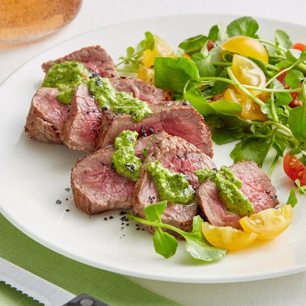 A plate of Rastelli's center cut top sirloin steak with green sauce and tomatoes.