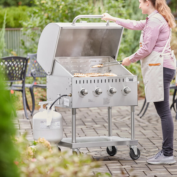 A woman wearing an apron cooking food on a Backyard Pro stainless steel outdoor grill.