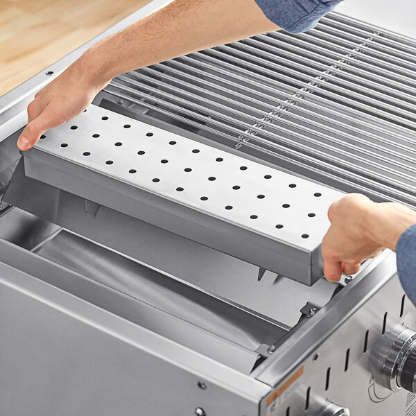 A person opening a metal tray on a grill with a Backyard Pro Smoker Box.