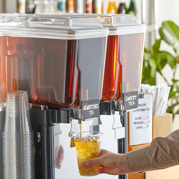 A person using a beverage dispenser to pour Tractor Beverage Co. Organic Unsweet Tea concentrate into a plastic cup with ice.