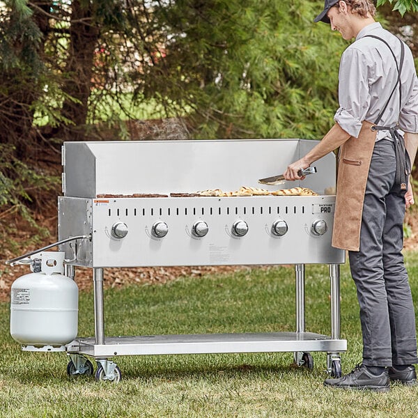 A man cooking food on a Backyard Pro grill with a wind guard.