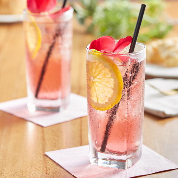 Two glasses of Tractor Beverage Co. Organic Hibiscus drink with pink liquid and straws on a table.