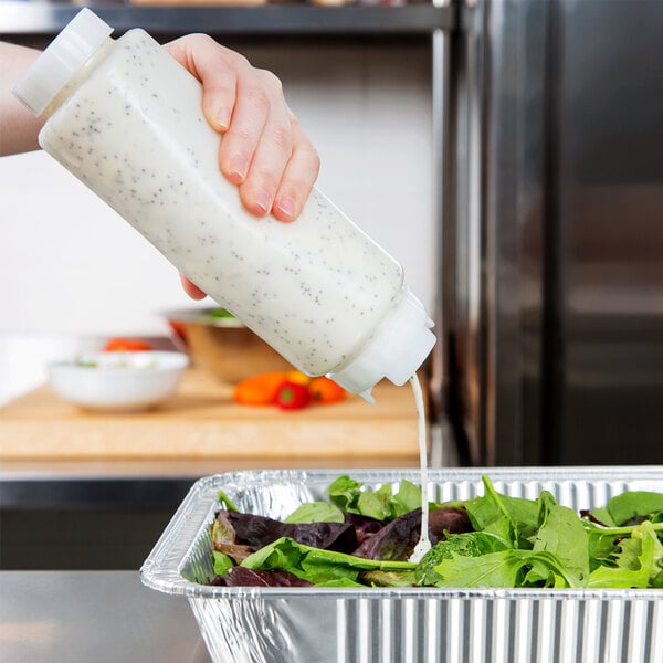 A person using a FIFO squeeze bottle to pour white liquid on a salad in a pan.