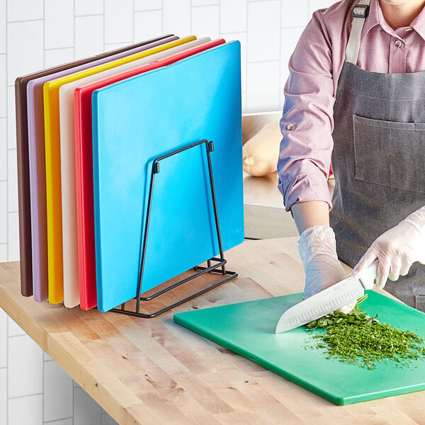 A woman cutting vegetables on a Choice polyethylene cutting board.
