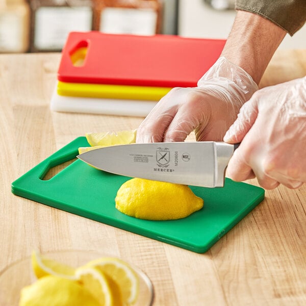 A person using a Choice polyethylene cutting board to cut a lemon.