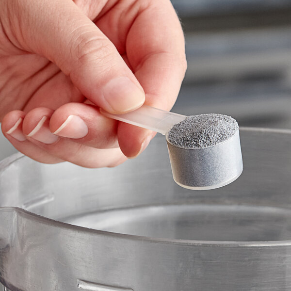 A hand using a 5 cc polypropylene scoop to measure grey powder.