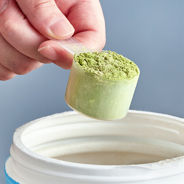 A hand using a 20 cc polypropylene scoop to pour green powder into a container.