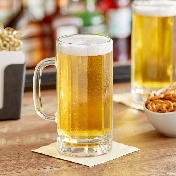 A glass mug of beer on a table with a bowl of pretzels.