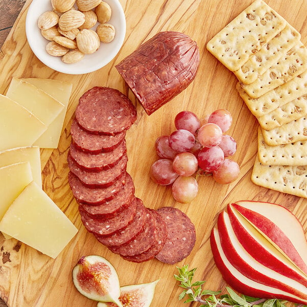 Slices of Shaffer Venison Farms water buffalo summer sausage on a wooden board with cheese, crackers, grapes, and nuts.