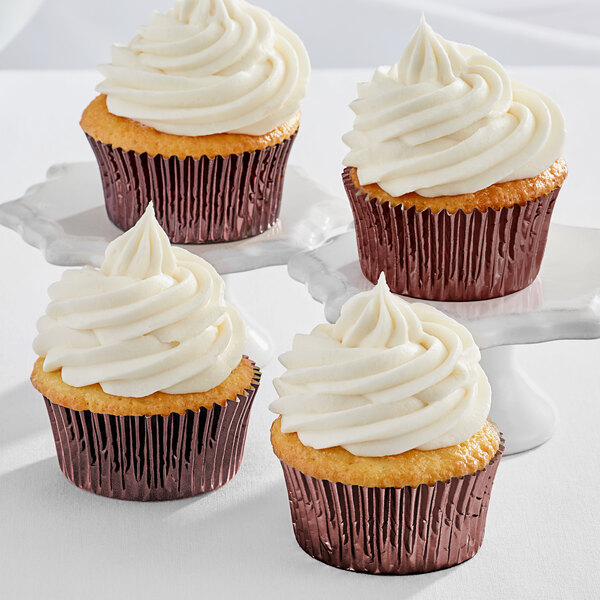 Three Enjay brown foil baking cups with cupcakes and white frosting on a white plate.