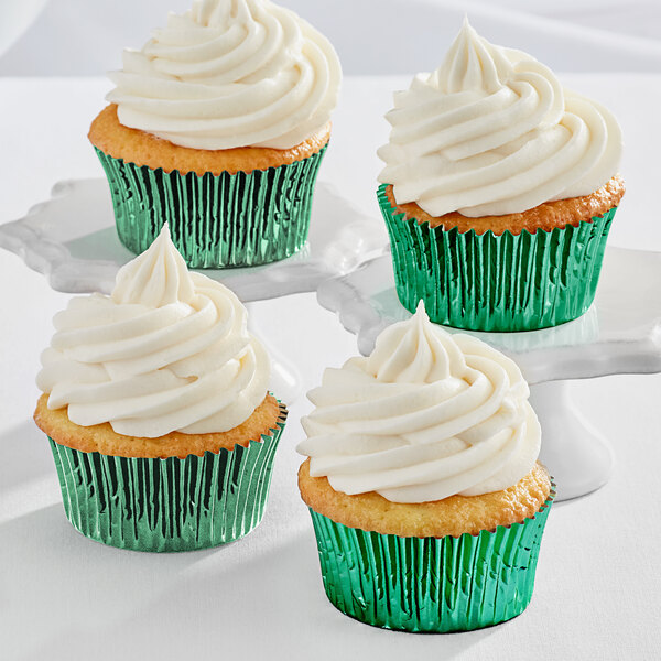 Three Enjay green foil cupcakes with white frosting on white plates.