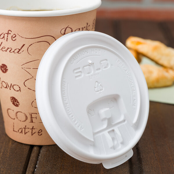 A Solo white plastic lid on a coffee cup with writing on it on a table next to a pastry.
