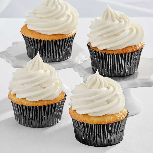 Three Enjay black foil baking cups with white frosting on cupcakes.