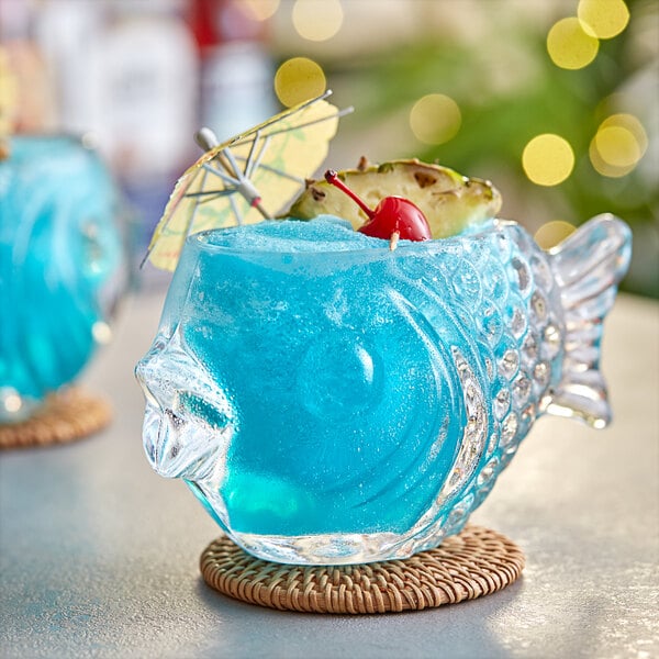 A blue cocktail in an Acopa fish shaped glass with a pineapple garnish.