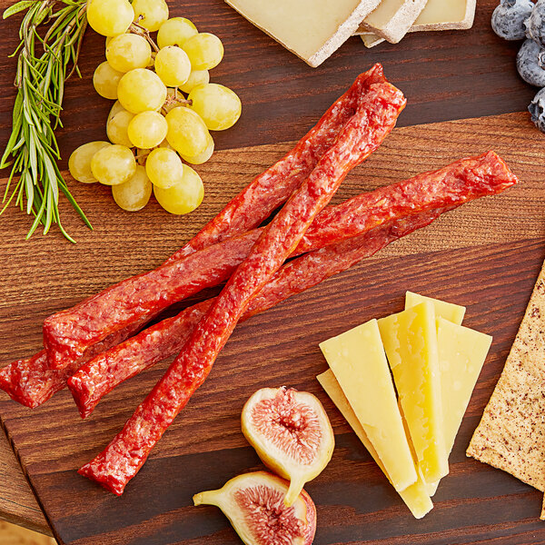 Smokey barbecue wild boar snack sticks on a wooden cutting board with cheese, grapes, and crackers.