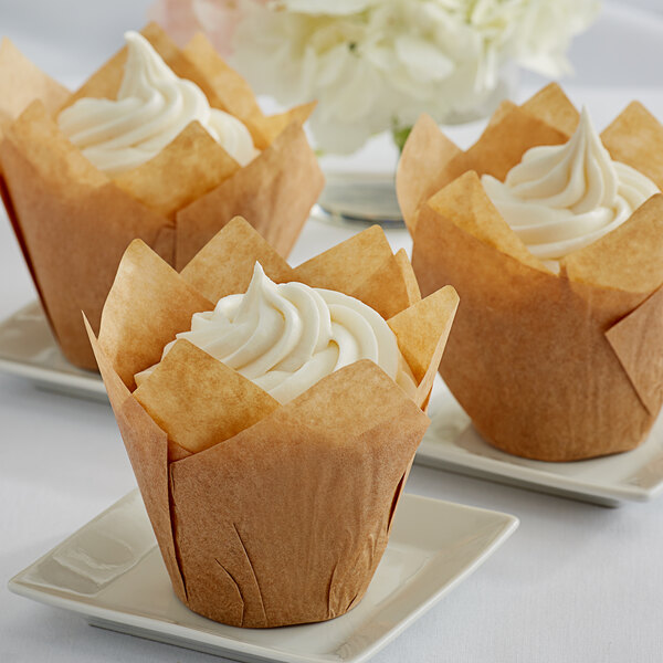 Three Enjay natural tulip baking cups with cupcakes on white plates.
