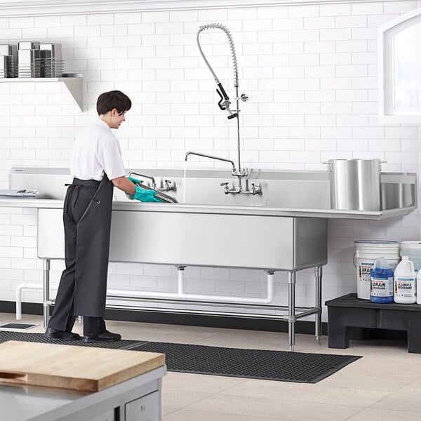 A person in an apron using a Regency stainless steel three compartment sink in a commercial kitchen.