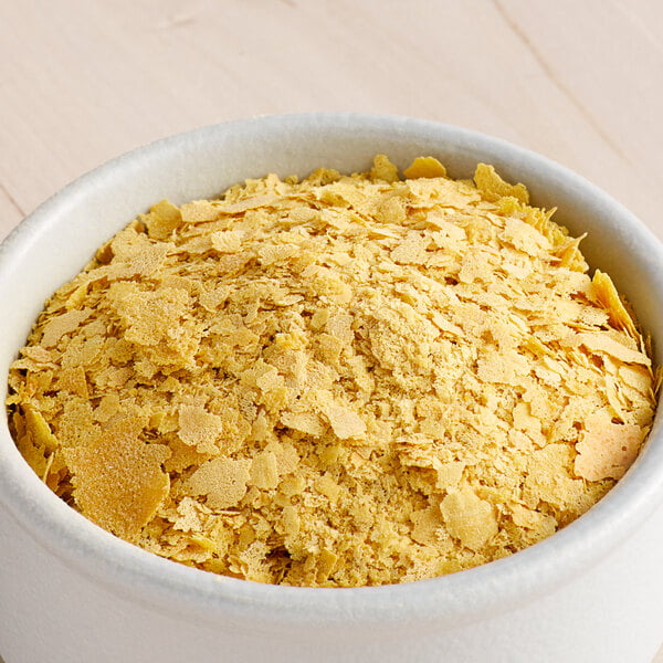 A white container filled with large nutritional yeast flakes.