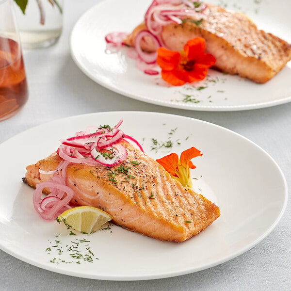 Two plates of Loch Duart Scottish salmon fillet with onions and lemon slices on a table.