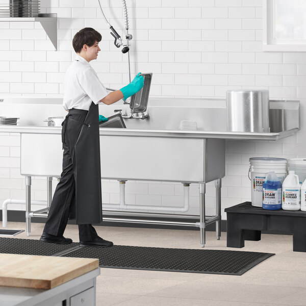 A man in a black apron using a Regency stainless steel three compartment commercial sink.