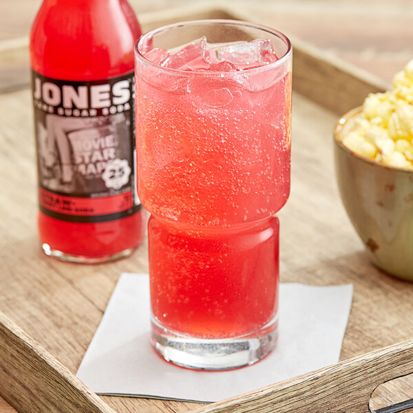 A glass of Jones strawberry lime soda next to a bowl of popcorn.