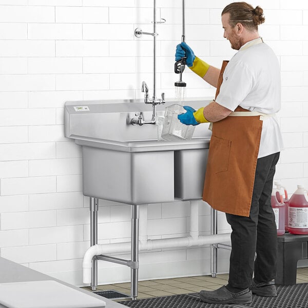 A man in a brown apron and orange gloves working in a Regency commercial 3 compartment sink.