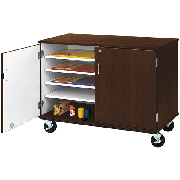 A dark brown slotted storage cart with shelves and a white door on wheels.
