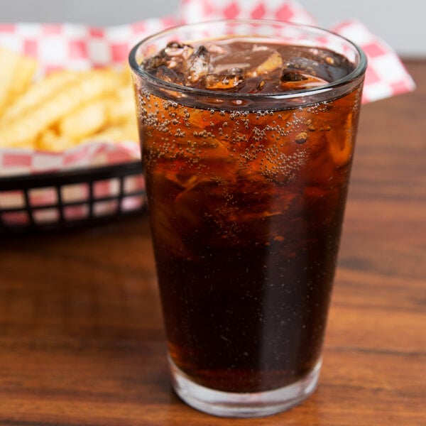 A Libbey customizable beverage glass filled with soda and ice on a table with a basket of fries.