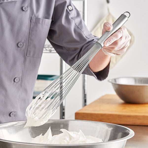 A person in a chef's uniform using a Choice stainless steel piano whisk to mix whipped cream in a bowl.