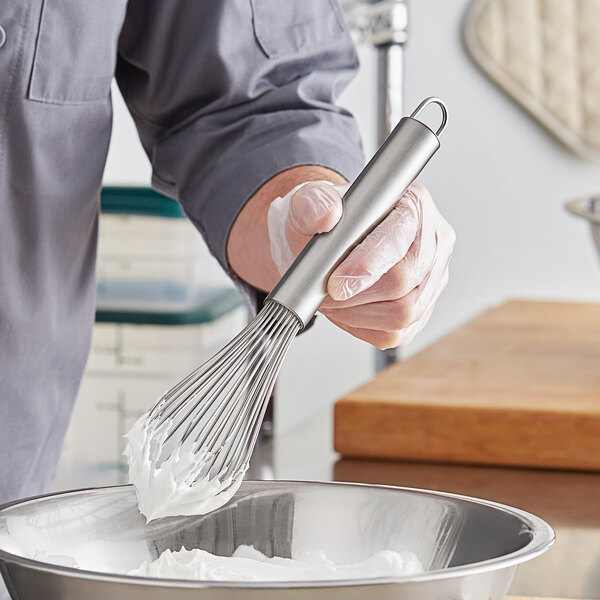 A person using a Choice stainless steel piano whisk to mix ingredients in a bowl.