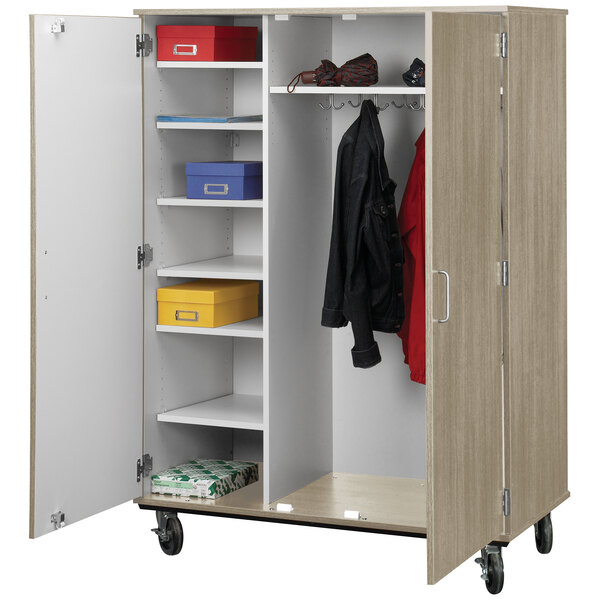 An I.D. Systems natural elm storage cart with locking doors filled with clothes and shoes.