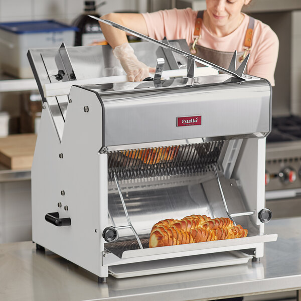 A woman in an apron and gloves slicing bread with an Estella countertop bread slicer.