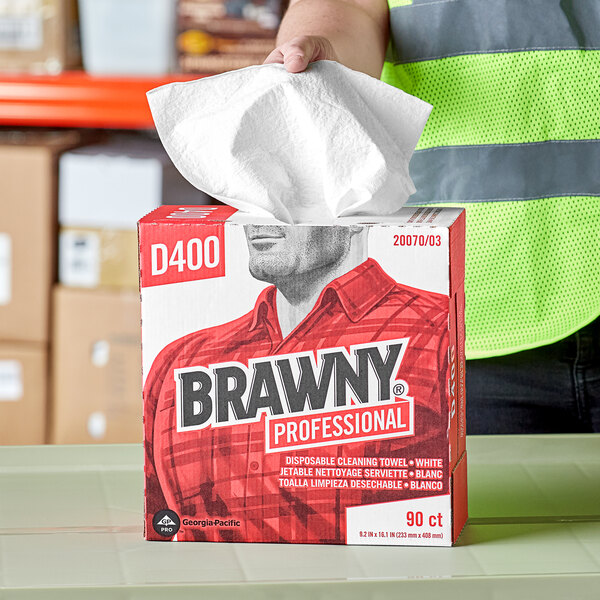 A man holding a box of Brawny Professional white tall box industrial cleaning towels.