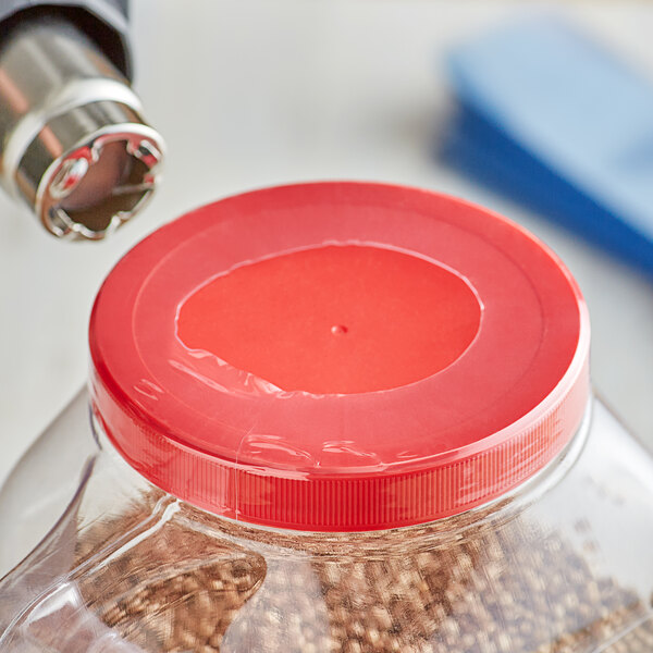 A person using a drill to shrink a clear plastic band around a container with a red lid.