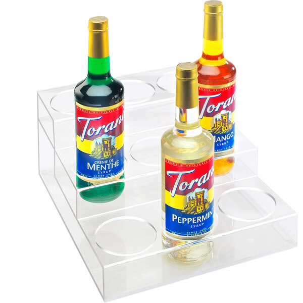A clear acrylic Cal-Mil bottle holder with three tiers holding bottles.