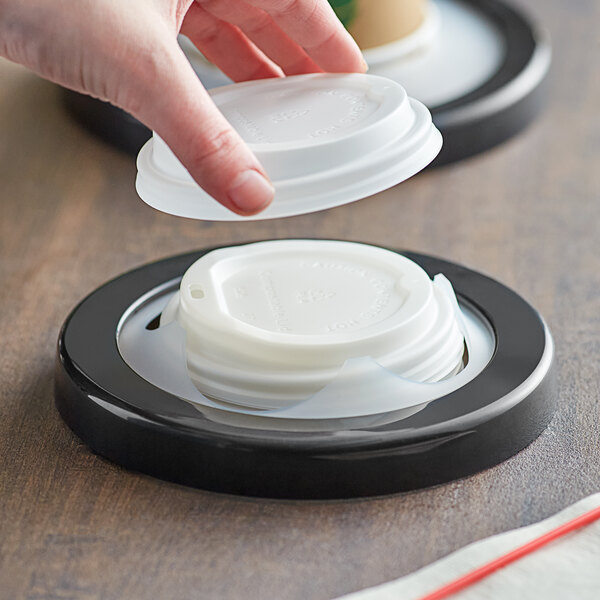 A hand using a San Jamar EZ-Fit In-Counter Lid Dispenser to put a plastic lid on a coffee cup.