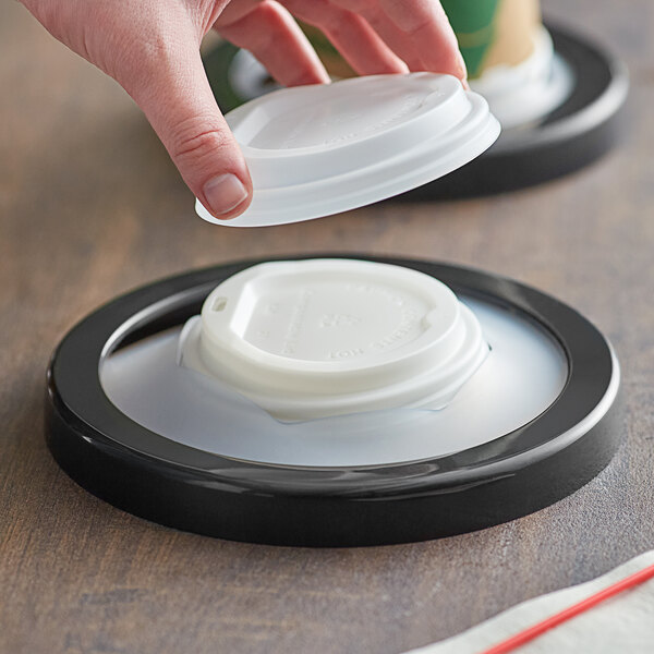 A hand using a San Jamar in-counter lid dispenser to put a white plastic lid on a coffee cup.