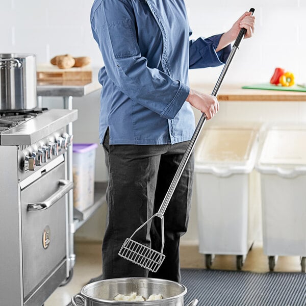 A woman in a chef's uniform using a Fourt&#233; stainless steel potato masher.