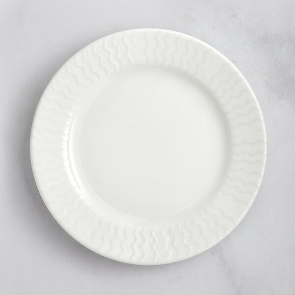 A close up of a white RAK Porcelain flat plate with wavy lines on the rim.
