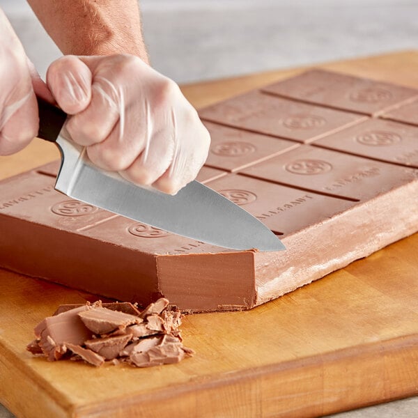 A person cutting a Callebaut milk chocolate block with a knife.