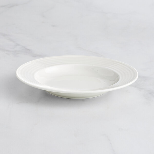 A RAK Porcelain ivory deep plate with an embossed wide rim on a marble surface.