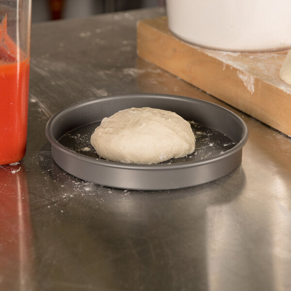 A ball of pizza dough in an American Metalcraft Hard Coat Anodized Aluminum pizza pan.