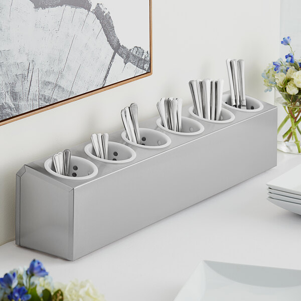 A stainless steel flatware organizer with white perforated plastic cylinders holding silverware.